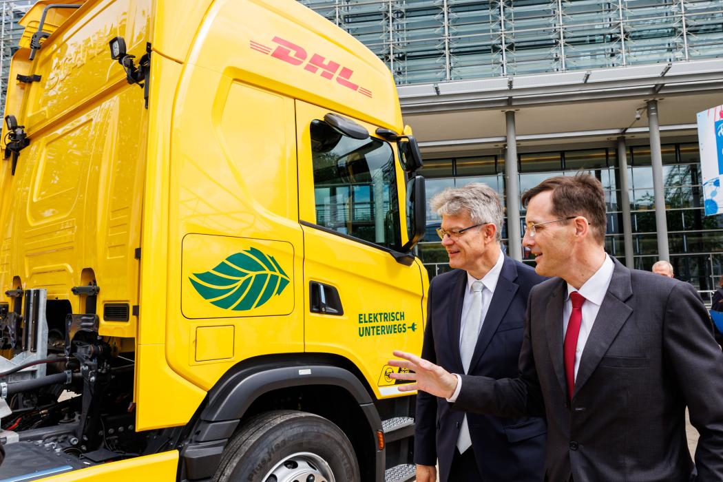 Tobias Meyer, CEO der DHL Group erklärt Bundesverkehrsminister Patrick Schnieder den batterieelektrischen Scania-Lkw mit Range Extender. | Bild: DHL